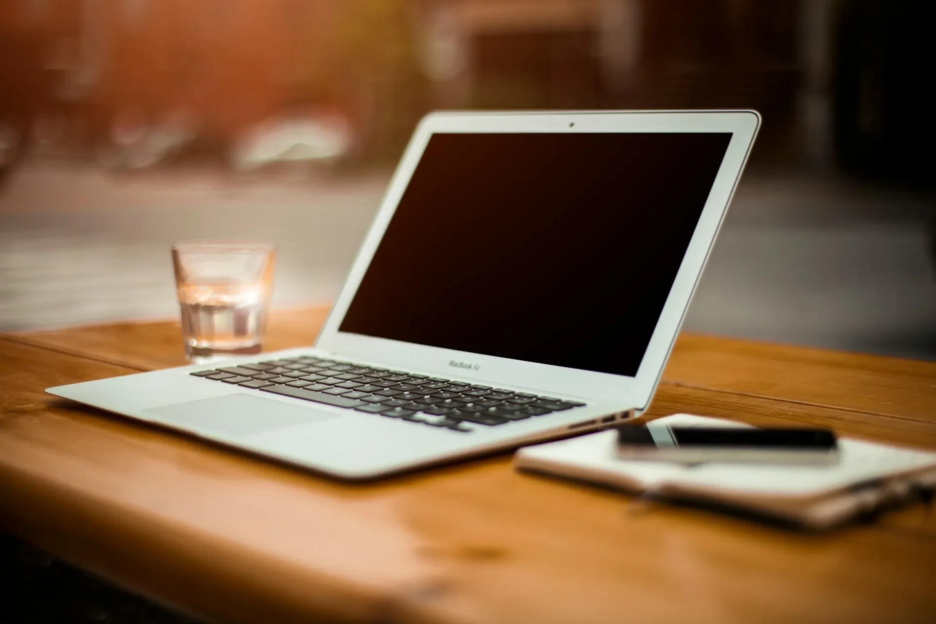Aufgeklappter Laptop auf Holztisch mit Wasserglas und Notizbuch