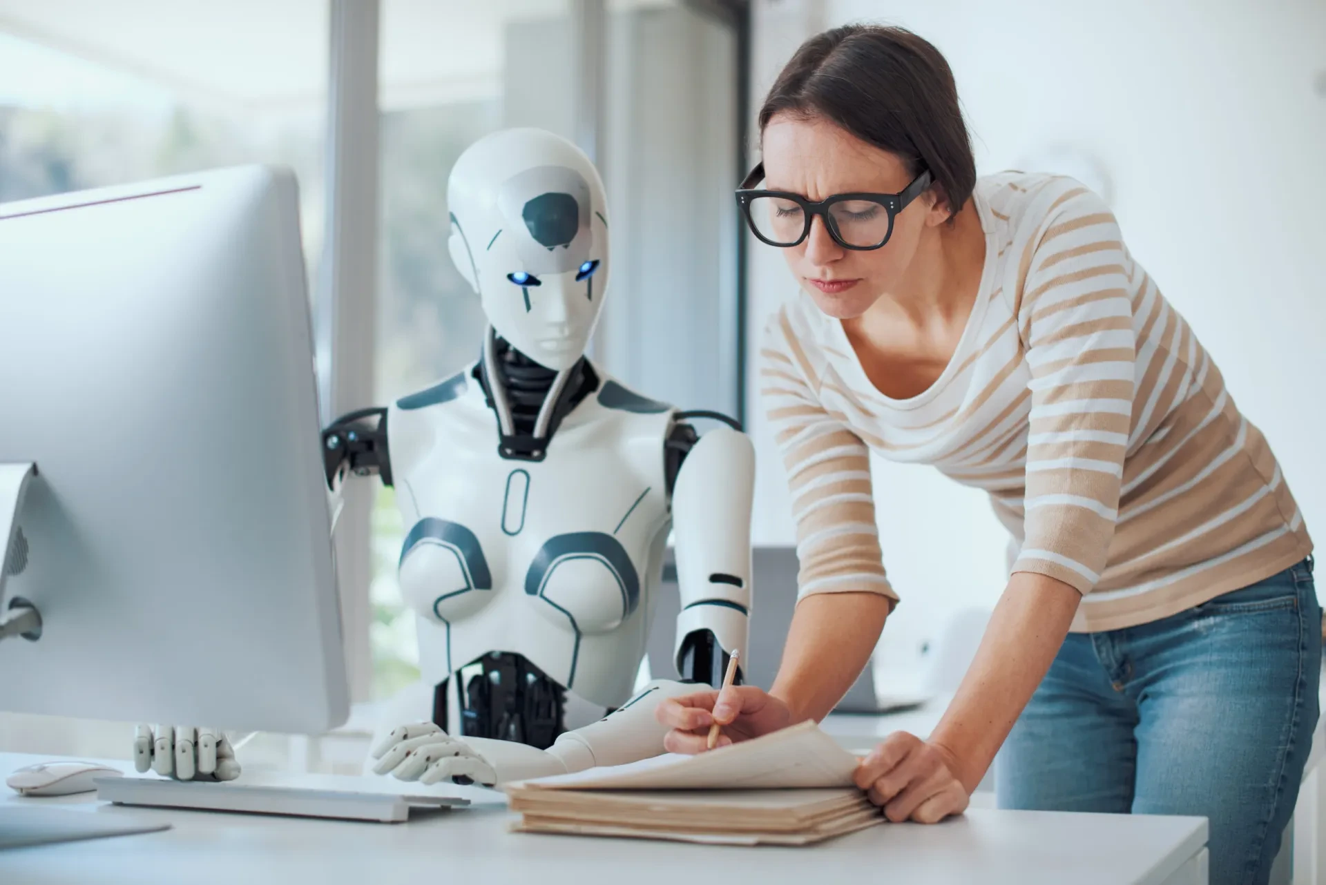 Frau mit Brille arbeitet gemeinsam mit einem humanoiden Roboter am Schreibtisch