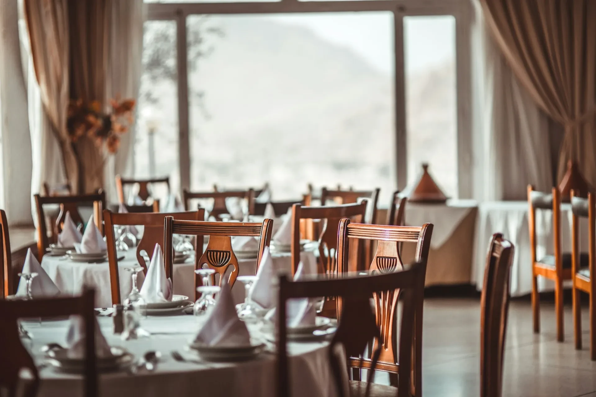 Gedeckte Tische mit weißen Tischdecken und Holzstühlen in einem leeren Restaurant