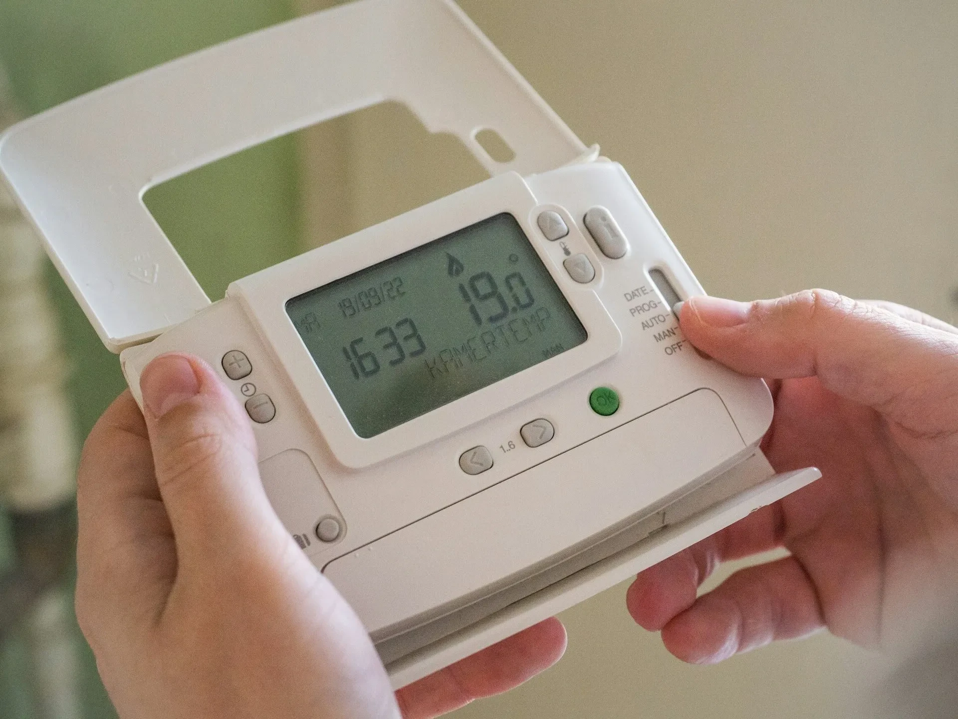 Person hält programmierbaren Thermostat mit digitaler Temperaturanzeige in den Händen