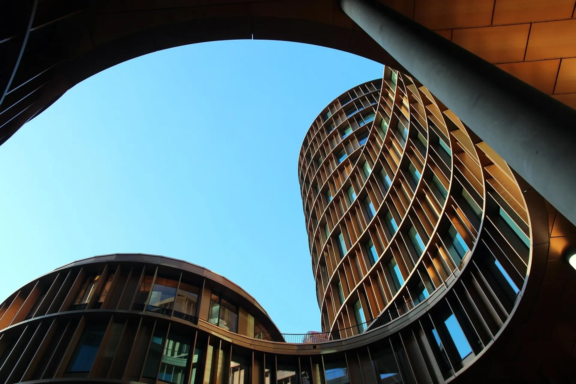Modernes rundes Hochhaus mit geschwungener Fassade von unten fotografiert vor blauem Himmel
