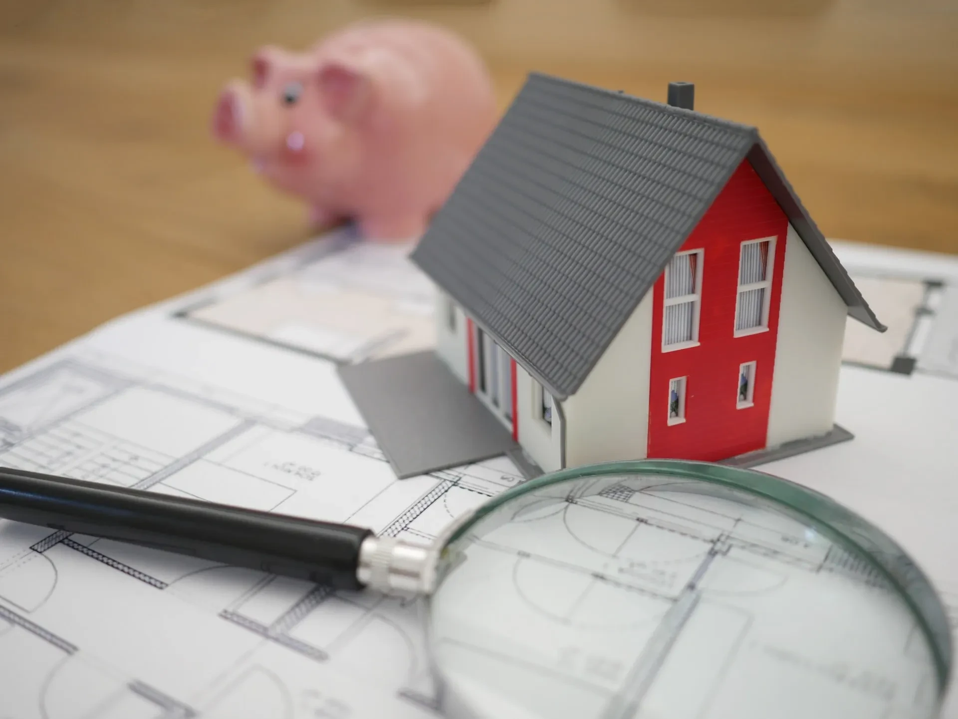 Miniaturhaus mit Lupe und Sparschwein auf Bauplan