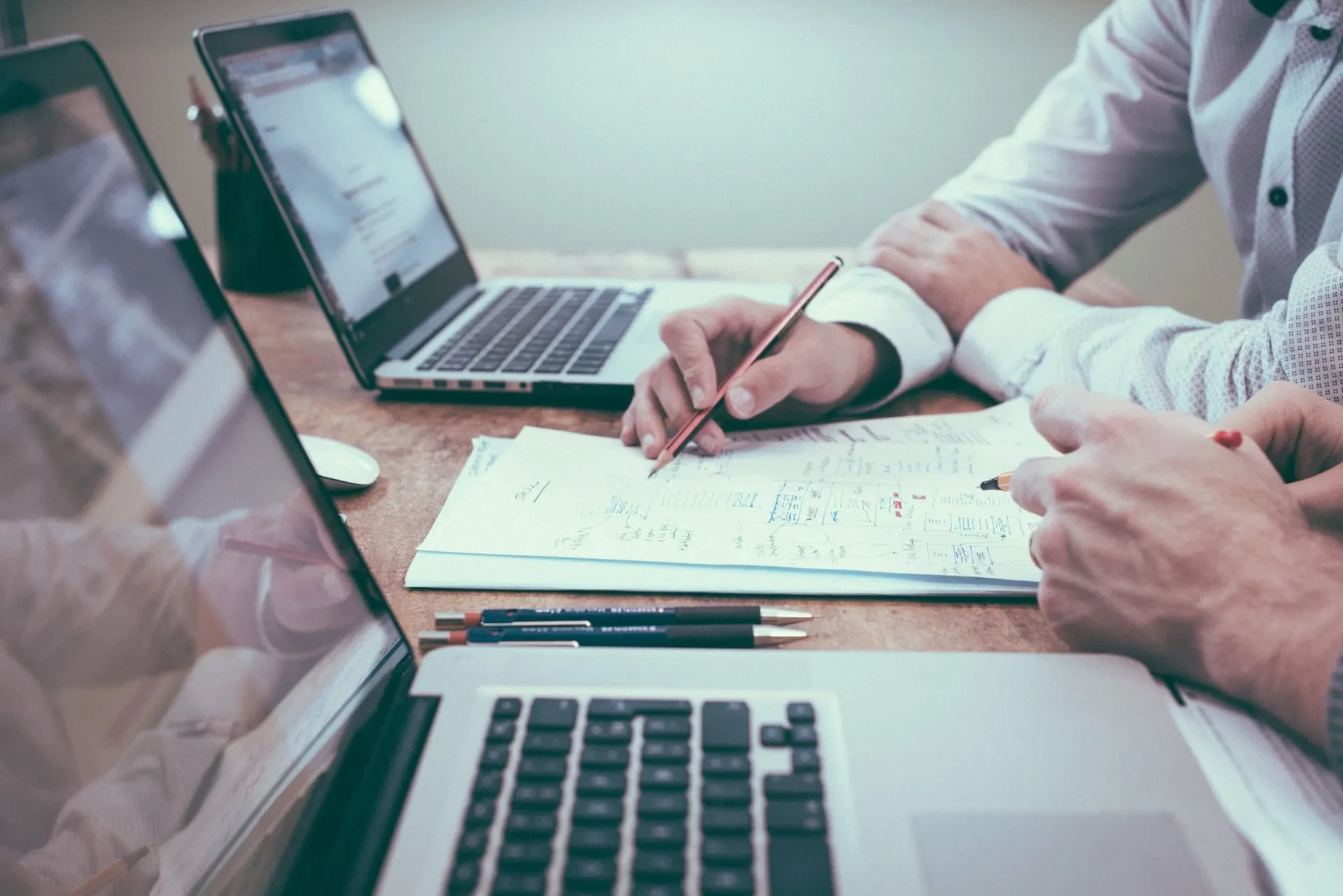 Zwei Personen arbeiten gemeinsam an Dokumenten mit Laptops auf dem Schreibtisch