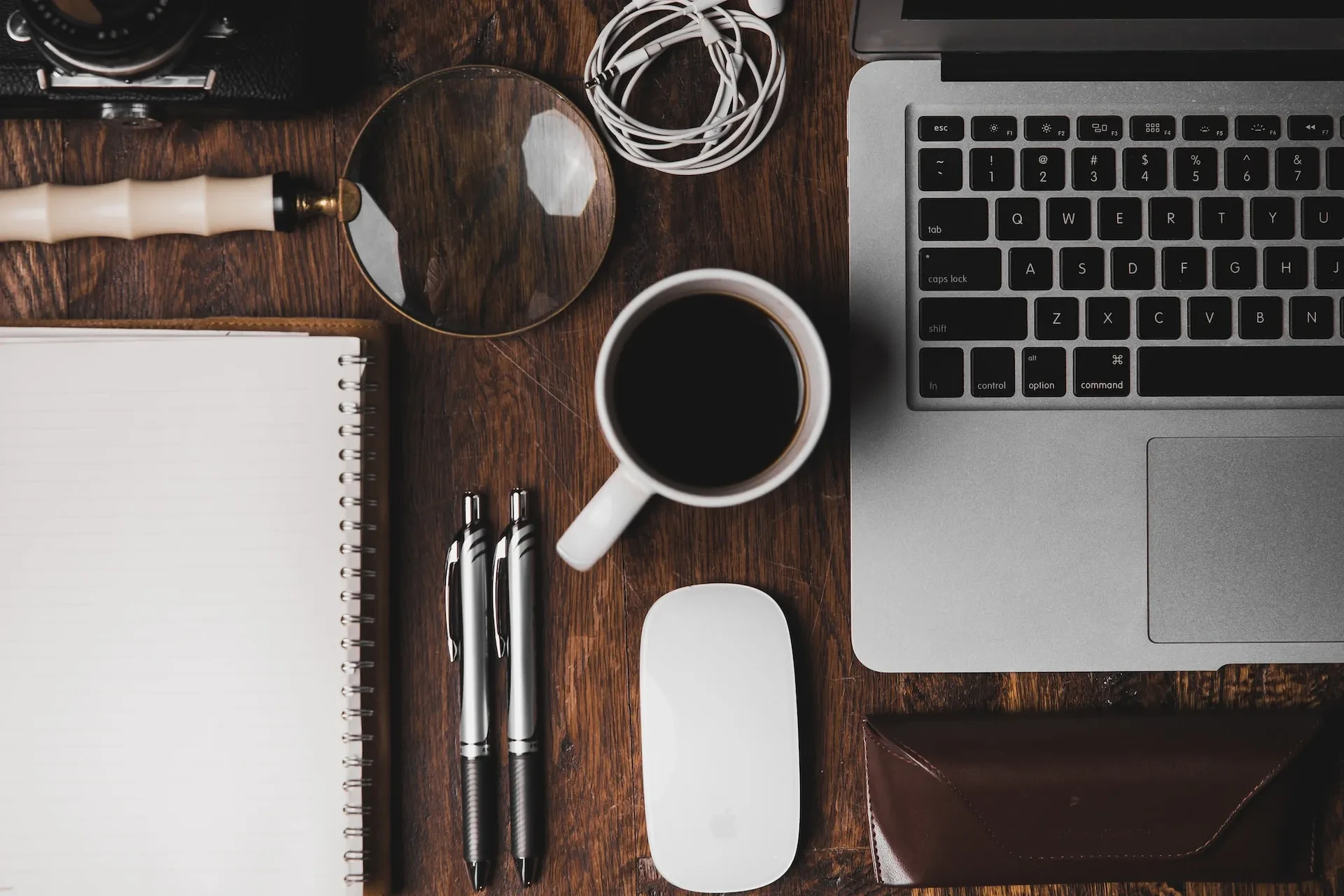 Schreibtisch von oben mit Laptop, Kaffeetasse, Notizbuch, Lupe und Stiften