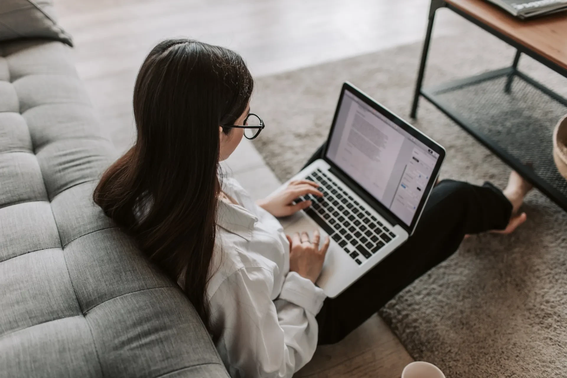 Person mit Brille arbeitet auf dem Boden sitzend am Laptop