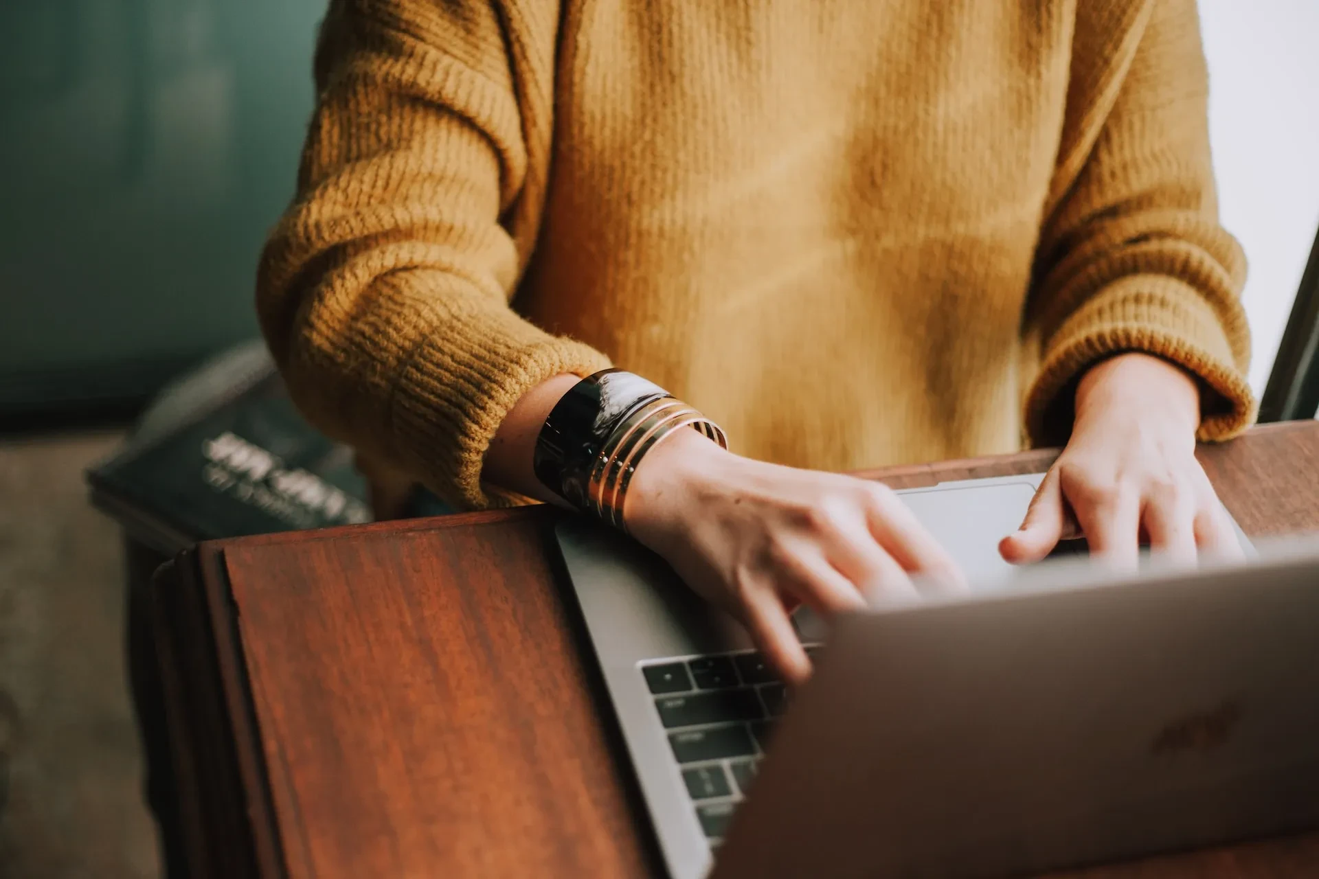 Person in gelbem Pullover tippt auf einem Laptop