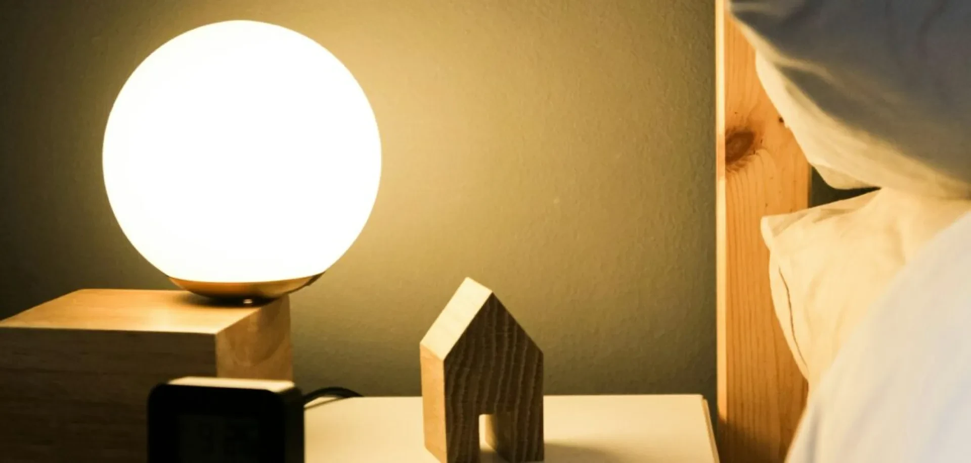 Nachttischlampe mit Holzsockel und kleines Holzhäuschen neben einem Bett